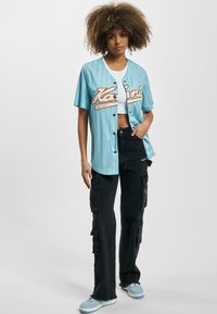 Maglietta da baseball a righe sottili di colore blu chiaro con bottoni bianchi e lettering arancione, abbinata a pantaloni cargo neri con molteplici tasche.
