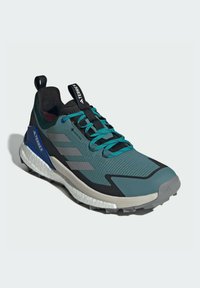 Men's trail running shoe in teal and black, featuring a textured upper, gray accents, and a rugged sole for traction. Gore-Tex for weatherproofing.