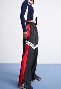 Nike sportswear featuring black pants with red side stripes, white accents, and zippers at the ankles, paired with a cropped navy and white jacket.