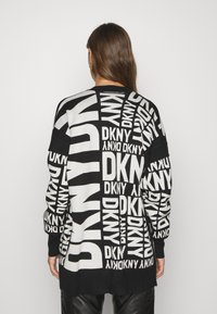 Svart och vit stickad tröja med ett upprepat "DKNY" logomönster, långa ärmar och en något längre bakdel.