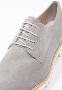 Chaussure à lacets en daim gris clair avec une semelle épaisse blanche et une bordure en bois, montrant les détails de l'avant et du côté.