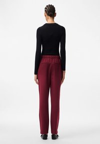 Svart ribbad långärmad topp i kombination med vinröda byxor med elastisk midja och två bakfickor, visad bakifrån.