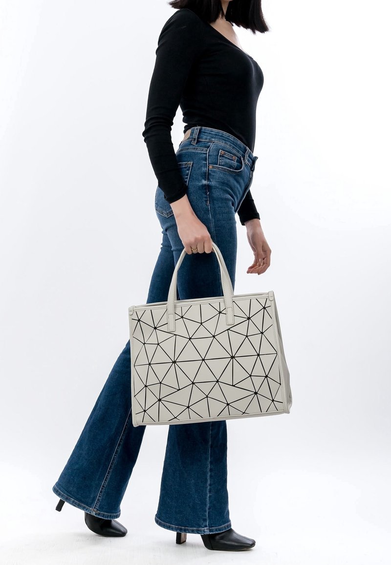 Sac cabas géométrique gris avec des motifs triangulaires noirs, en cuir lisse, doté de deux poignées supérieures, conception spacieuse, porté avec un jean évasé bleu.