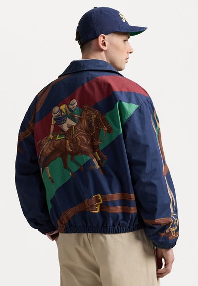 Veste navy avec un graphisme de course de chevaux, comportant des rayures diagonales rouges, vertes et bleues, des poignets élastiques et une taille cintrée.