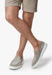 Graue Wildleder-Slipschuhe mit einer weißen Gummisohle, die eine glatte Textur und ein minimalistisches Design aufweisen, platziert neben beigen Shorts.