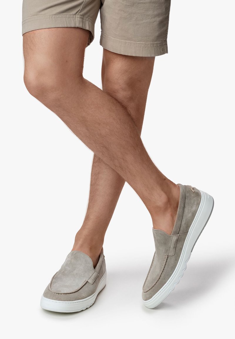 Graue Wildleder-Slipschuhe mit einer weißen Gummisohle, die eine glatte Textur und ein minimalistisches Design aufweisen, platziert neben beigen Shorts.