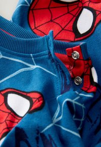 Modré flísové pyžamo s červenými motívmi Spider-Mana, s okrúhlym výstrihom a patentkami na golieri pre jednoduché obliekanie.