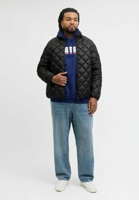 Czarna pikowana kurtka puchowa z zamkiem, noszona na niebieskiej bluzie z kapturem, w zestawieniu z jasnoniebieskimi dżinsami i białymi sneakersami. Prosty, nowoczesny design.