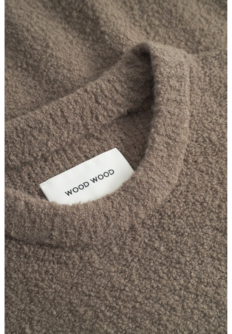 Pull en polaire marron avec un décolleté arrondi. La texture est douce et duveteuse. Une étiquette portant la mention "WOOD WOOD" est visible dans la zone du décolleté.