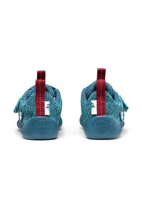 Zapatos de tela en color turquesa con un diseño texturizado. Presentan tiradores rojos, correas de Velcro y una suela ligera azul con estampado de logo.