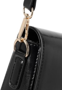 Esquinas de un bolso de cuero negro con herrajes de metal dorado y cierre. Costura detallada visible en el borde, textura suave.