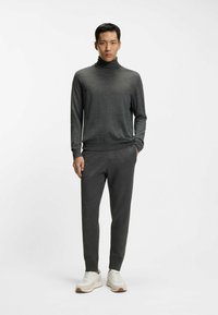 Ciemnoszary golf z długimi rękawami, w zestawie z dopasowanymi spodniami. Materiał wydaje się miękki, z lekkim połyskiem. Białe trampki z akcentami.