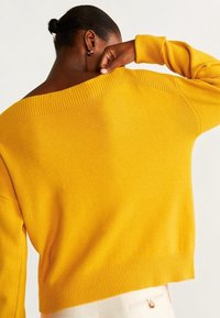 Senfgelber Strickpullover mit weitem Ausschnitt, gerippten Bündchen und Saum. Verfügt über eine übergroße Passform und eine weiche Textur.