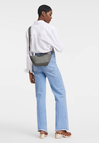 Grau gesteppte Umhängetasche mit gewölbter Form, verstellbarem Trageriemen und einem kleinen Frontverschluss, kombiniert mit hellblauen Jeans und einem weißen Hemd.