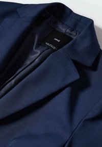 Blazer bleu marine en tissu lisse, doté d'un col classique et d'une doublure en satin, avec une étiquette cousue à l'intérieur. Design simple et épuré.