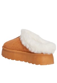 Zapatilla de ante marrón con un borde de piel de pelo blanco y una suela gruesa y texturizada. Presenta una punta redondeada y un diseño abierto para facilitar su uso.