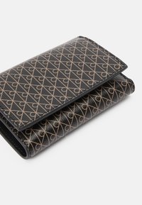 Čierny peňaženka s geometrickým vzorom srdca v béžovej farbe. Vyrobená z textúrovaného materiálu s preklápacím dizajnom a hladkými okrajmi.