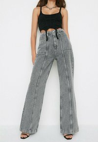 Jean taille haute, large, en denim gris clair avec des coutures contrastantes noires. Associé à un haut noir court et des sandales à talons hauts noires.