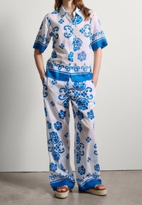 Witte linnen shirt- en broekset met blauwe bloemenpatronen en contrasterende blauwe afwerking. Losse pasvorm, korte mouwen en brede pijpen.