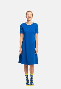 Blaues, kurzärmeliges Kleid mit fließendem Rock, aus glattem Stoff. Kombiniert mit gelben Socken mit Bananamuster.
