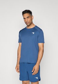 Blaues Sporthemd und Shorts aus feuchtigkeitsableitendem Material. Mit Rundhalsausschnitt, kurzen Ärmeln und einem weißen Logo auf der Brust.