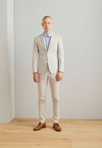 Traje gris claro con un diseño ajustado, complementado con una camisa azul claro. Zapatos de cuero marrón, de textura minimalista y suave.