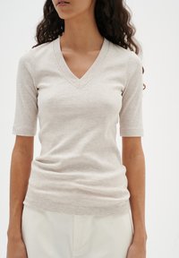 Hellbeige gerippter V-Ausschnitt-Top mit kurzen Ärmeln, das einen figurbetonten Schnitt und eine glatte Textur aufweist, ideal für legere Anlässe.