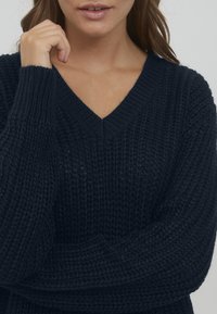 Maglione lavorato a maglia blu navy con scollatura a V, caratterizzato da un motivo testurizzato e polsini a coste. Materiale morbido con vestibilità comoda.