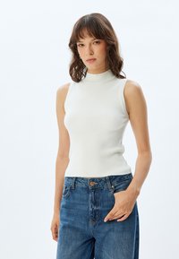 Top blanco sin mangas, de canalé y con cuello alto, combinado con jeans de tiro alto en un tono azul desgastado. Textura suave y diseño ajustado.