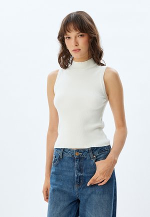 Top blanco sin mangas, de canalé y con cuello alto, combinado con jeans de tiro alto en un tono azul desgastado. Textura suave y diseño ajustado.