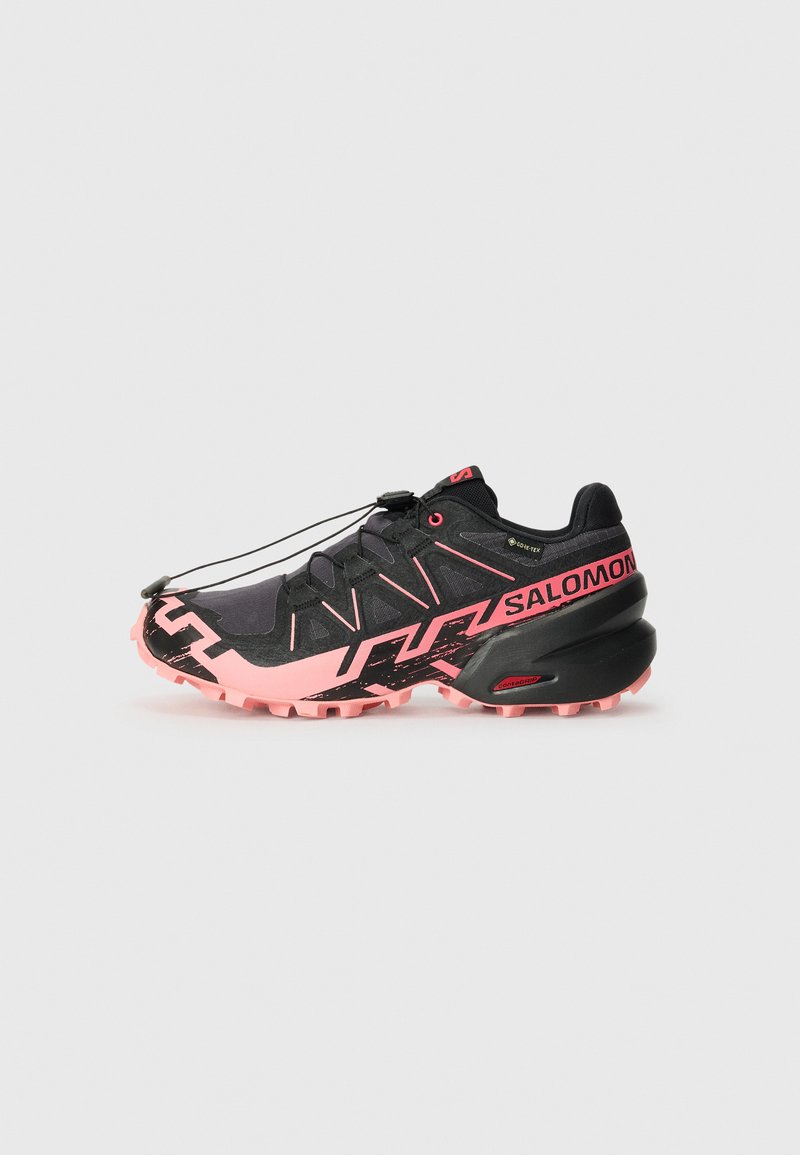 Chaussures de trail de course noires et roses avec une tige en mesh, une semelle intermédiaire texturée, un système de laçage prominent et une traction agressive sur la semelle extérieure.