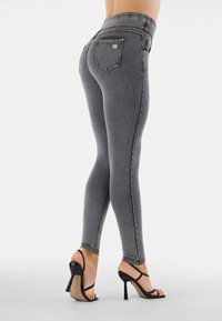 Harmaat korkeavyötäröiset leggingsit, kapealla istuvuudella, joissa on etu- ja takataskut, ommellut yksityiskohdat ja sileä pinta. Mustat remmikkäät korkokengät.