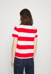 Punavalkoraidallinen lyhythihainen t-paita, jossa on pyöreä kaula-aukko, yhdistetty tummiin farkkuihin. Pehmeä puuvillainen pinta, rento istuvuus.