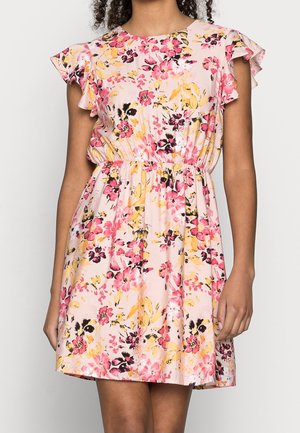 Kukkamekko vaaleanpunaisella taustalla, lyhyillä röyhelösateilla, elastisella vyötäröllä ja värikkäillä kukilla vaaleanpunaisissa, keltaisissa ja mustissa kuvioissa.