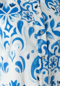 Blau-weißer Stoff mit floralen und abstrakten Mustern, einer glatten Textur und kleinen metallischen Knöpfen entlang der Vorderseite.