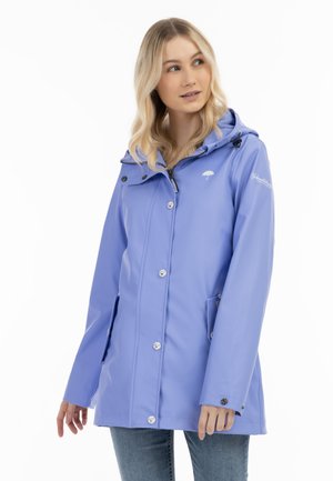 Frau trägt eine hellviolette Regenjacke mit Kapuze, Knöpfen und Reißverschluss vorne, steht vor einem weißen Hintergrund.