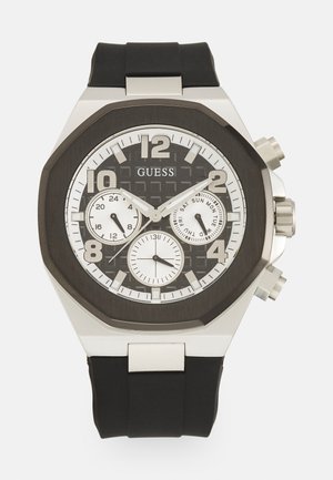 Men's Guess watch with an octagonal stainless steel case, black rubber strap, dark patterned dial, large silver numbers, and three sub-dials.