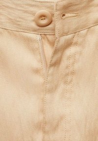Beige denim stof met een knoopsluiting, ritssluiting en details van zijnaadstiksel. Textuur met een zachte, gladde uitstraling.