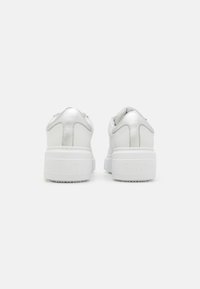 White leather sneakers with a chunky white sole. Features stitched accents and embossed branding on the heel. Smooth texture, minimal design.