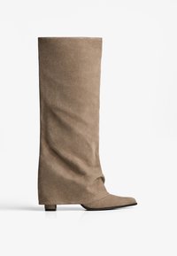 Tall beige suede boot with a low block heel and slightly slouched shaft, angled side view on a white background.