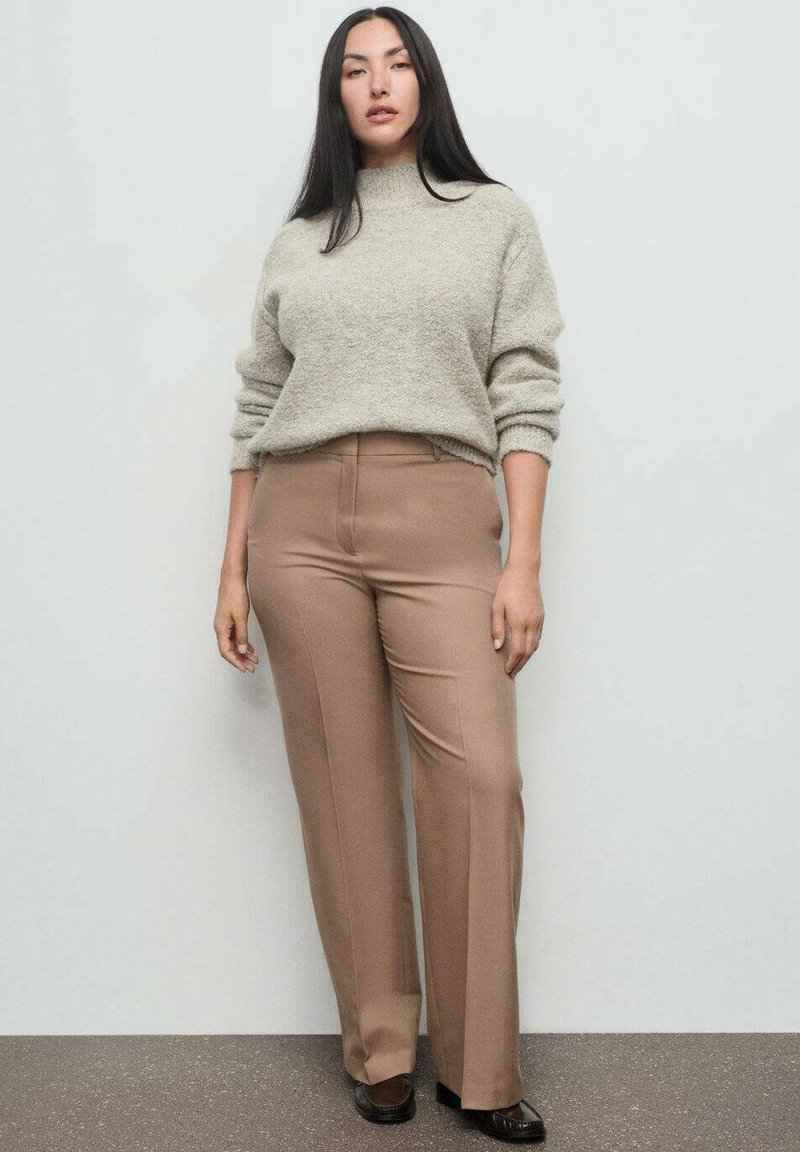Suéter de lana beige con cuello vuelto, de corte relajado. Pantalones marrones a medida con una textura suave y pierna recta. Zapatos negros planos.
