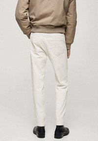 Pantaloni in denim bianco slim fit, con design a cinque tasche e tessuto leggermente testurizzato, abbinati a scarpe in pelle nere.
