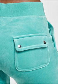 Turkusowe spodnie dresowe o miękkiej fakturze, z tylnią kieszenią zapinaną na zatrzask oraz ściągaczem w talii.