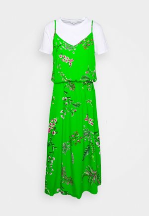 Robe midi fleurie verte avec un superposé à bretelles spaghetti sur une chemise blanche à manches courtes, avec divers motifs et une silhouette fluide.