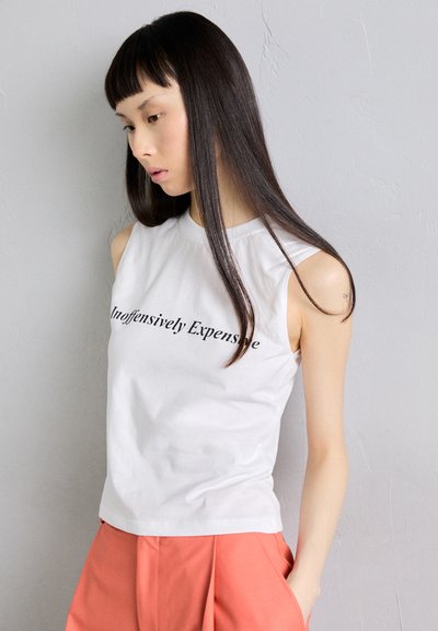 White sleeveless cotton top featuring the text "Unoffensively Expensive" in black, paired with peach-colored pleated pants.