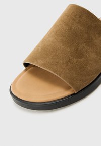 Sandale à glissière en daim marron avec une large bande supérieure, semelle intérieure rembourrée beige et semelle en caoutchouc noir texturé. Fini lisse sans motifs supplémentaires.