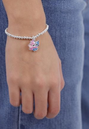 Braccialetto con perline argentate, caratterizzato da un charm a forma di personaggio dei cartoni animati rosa e blu, indossato su una mano su uno sfondo di denim.