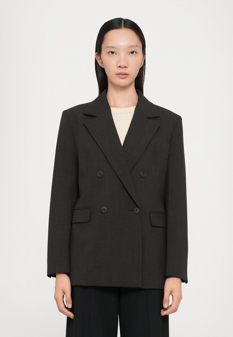 Blazer doppiopetto marrone scuro con rever a punta, due tasche a patta e bottoni neri. Vestibilità sartoriale con maniche dritte.