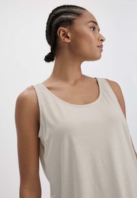 Top in beige chiaro realizzato in un tessuto morbido e liscio. Presenta una scollatura a giro e spalline larghe, con una silhouette rilassata e senza modelli visibili.