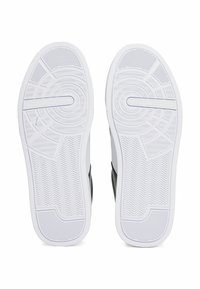 Sole di sneaker in bianco e nero realizzate in materiale gommoso con un pattern testurizzato e un distintivo design a spina di pesce. Presente il marchio “TOMMY HILFIGER”.